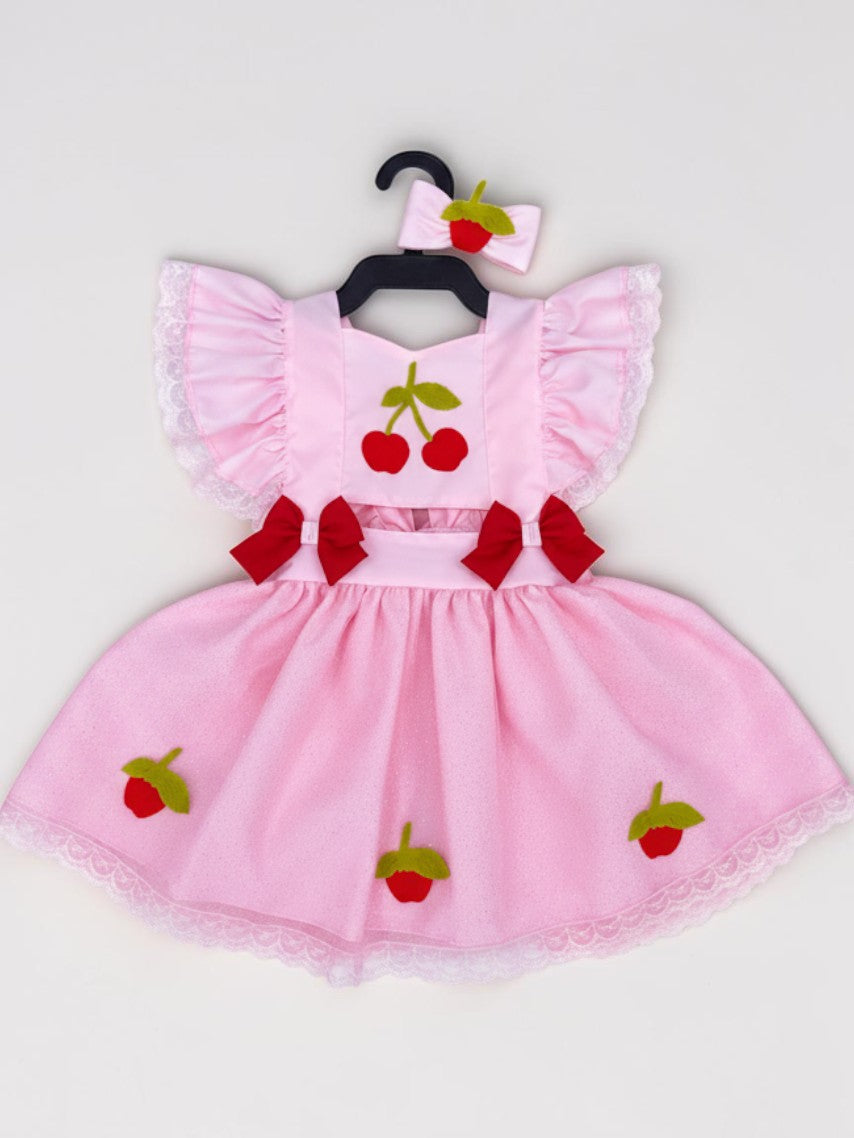 Romper vestido rosa Flor e Pipoquinha com estampa de cerejas, laços vermelhos, saia de tule e laço de cabelo a condizer.